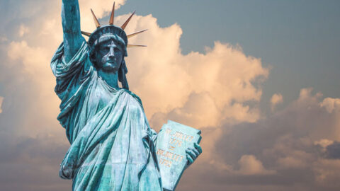 A close up of the iconic Statue of Liberty in New York City with background skies of patchy clouds.