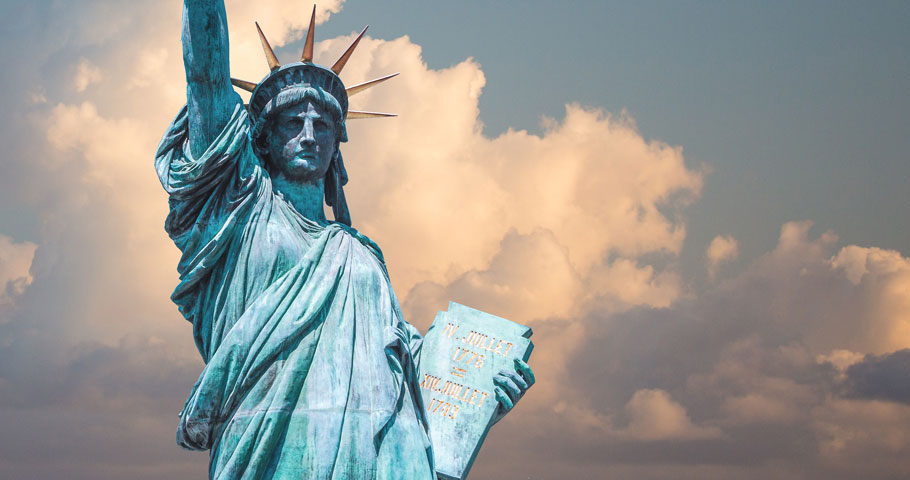 A close up of the iconic Statue of Liberty in New York City with background skies of patchy clouds.