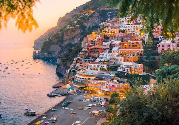 A colorful cliffside Italian village at dusk. The image is framed by overhanging vegetation.