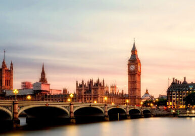 View across the Thames River overlooking West Minster Bridge and Big Ben, against pink skies at dusk.